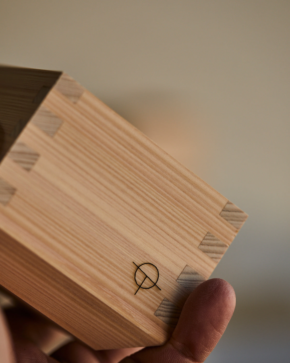 Hinoki sake cup held in the hand, corner joints catching the light